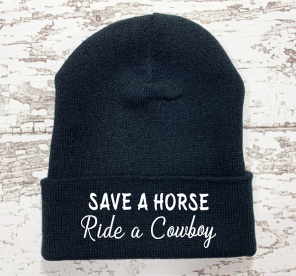 Black beanie with 'Save a Horse Ride a Cowboy' text on a wooden surface